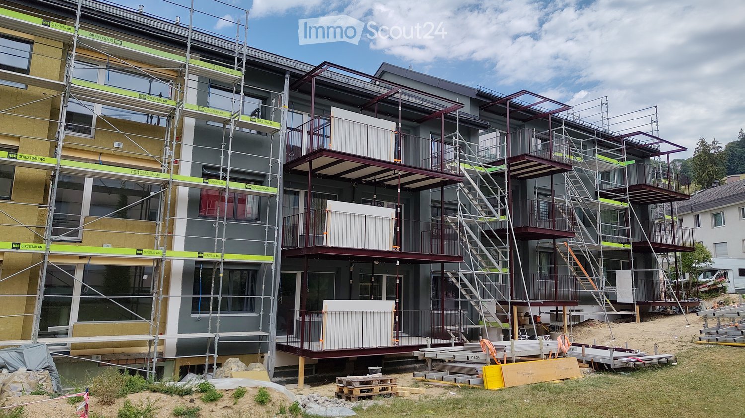 Multi-story residential building under construction with scaffolding, exposed steel beams, and unfinished balconies.