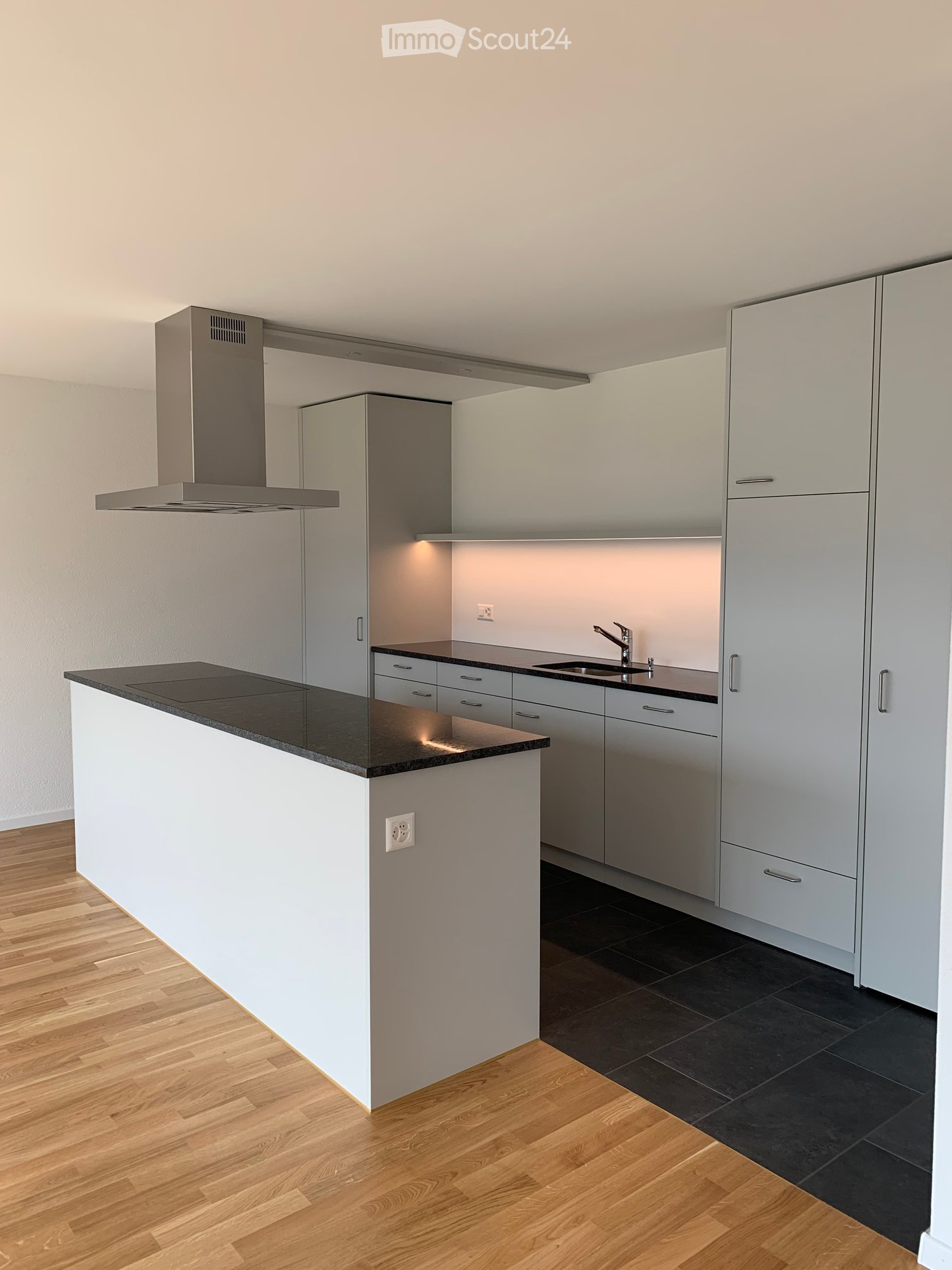 Modern kitchen with white cabinets, black countertops, a central island, and a stainless steel range hood.