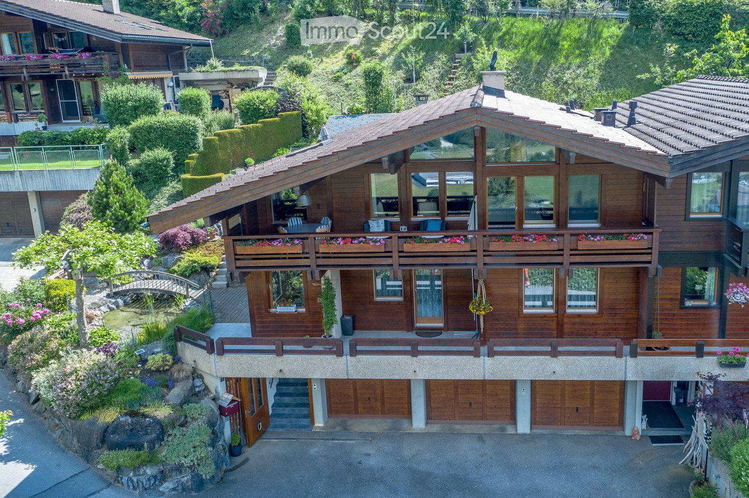 A two-story wooden house with large windows, balconies, and a well-maintained garden.