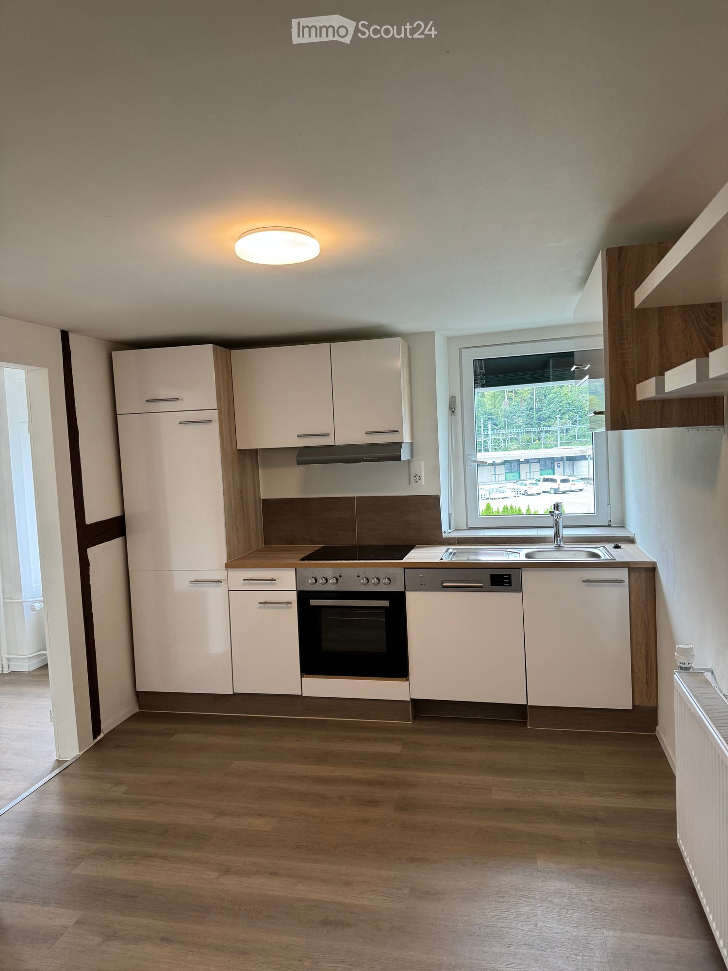 Modern kitchen with white cabinets, stainless steel appliances, wooden countertops, and a large window overlooking a parking area.