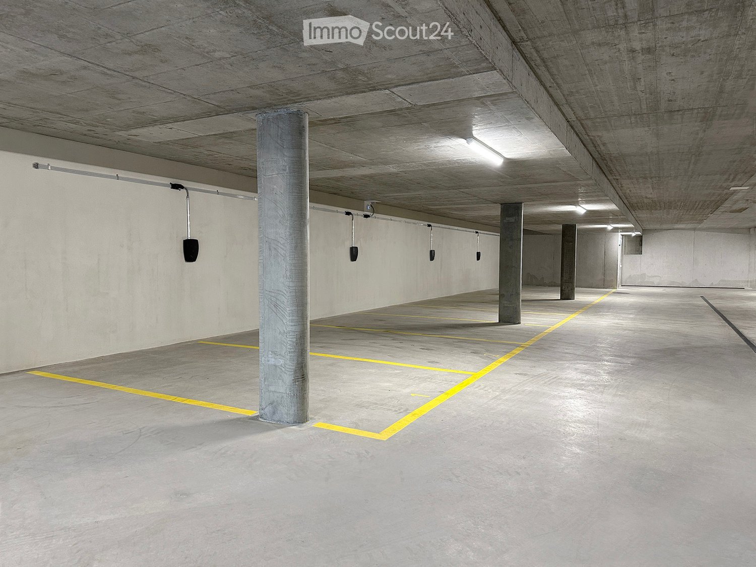 Empty underground parking area with concrete pillars, marked parking spaces, and overhead lighting.
