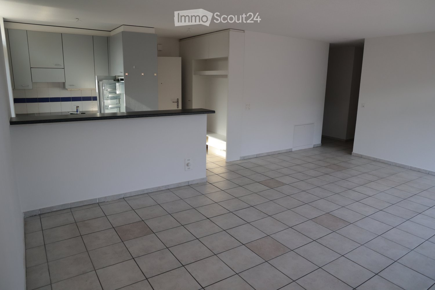 Empty kitchen area with tiled floor, white walls, grey cabinets, and a black countertop. No furniture or appliances are present.