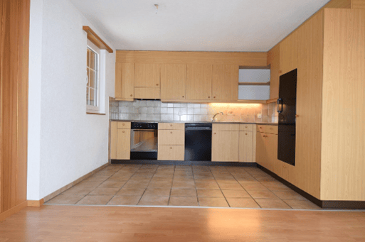 Modern kitchen with light wooden cabinets, stainless steel appliances, tiled backsplash, and wooden flooring.