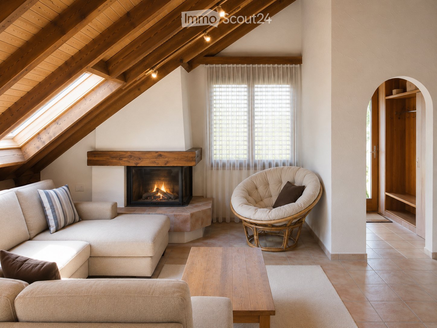 Cozy living room with exposed wooden beams, a lit fireplace, a sectional sofa, a wicker chair, and a coffee table.
