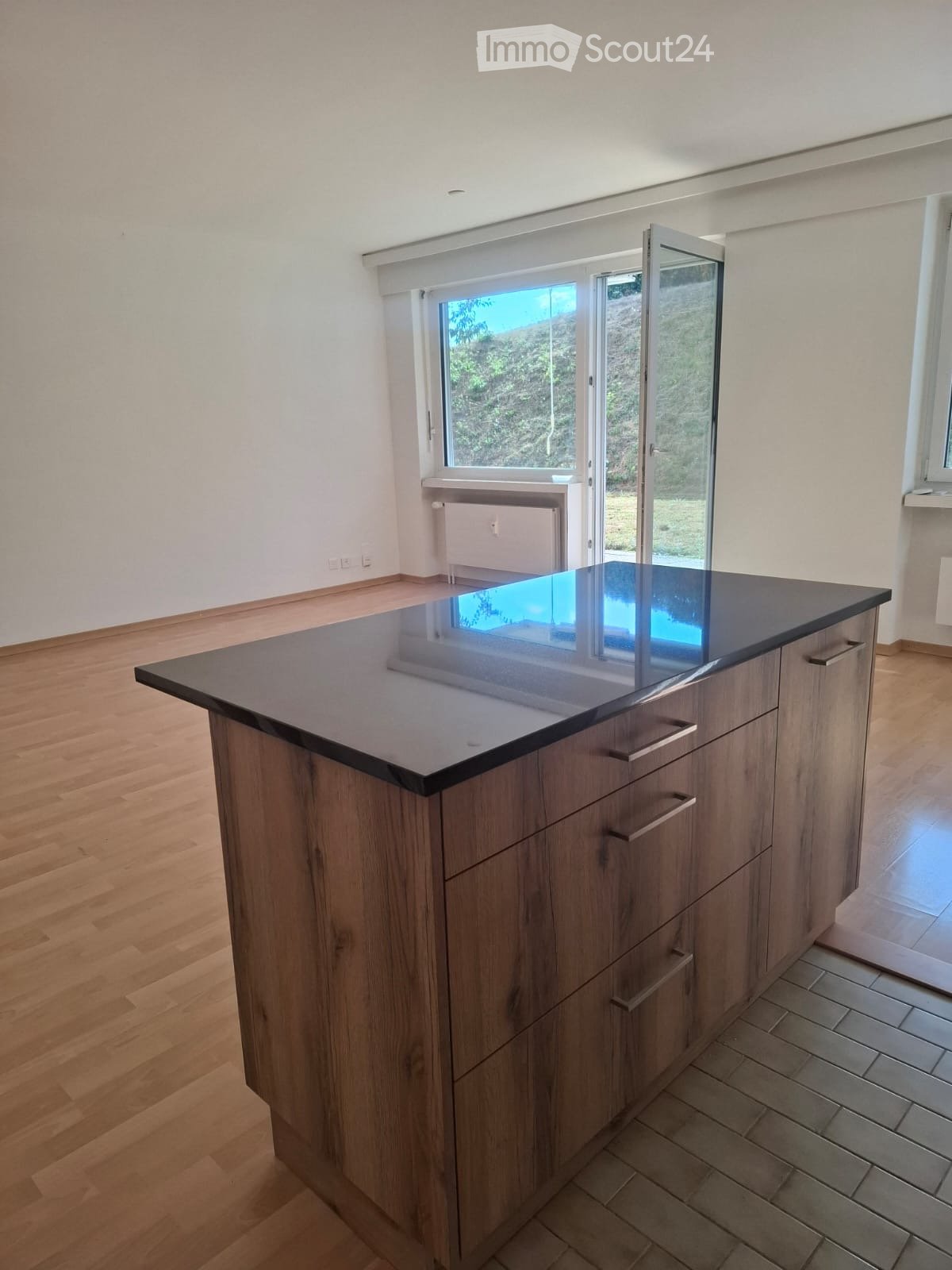 Modern kitchen with a wooden island and dark countertop, large windows and sliding doors leading to a garden.