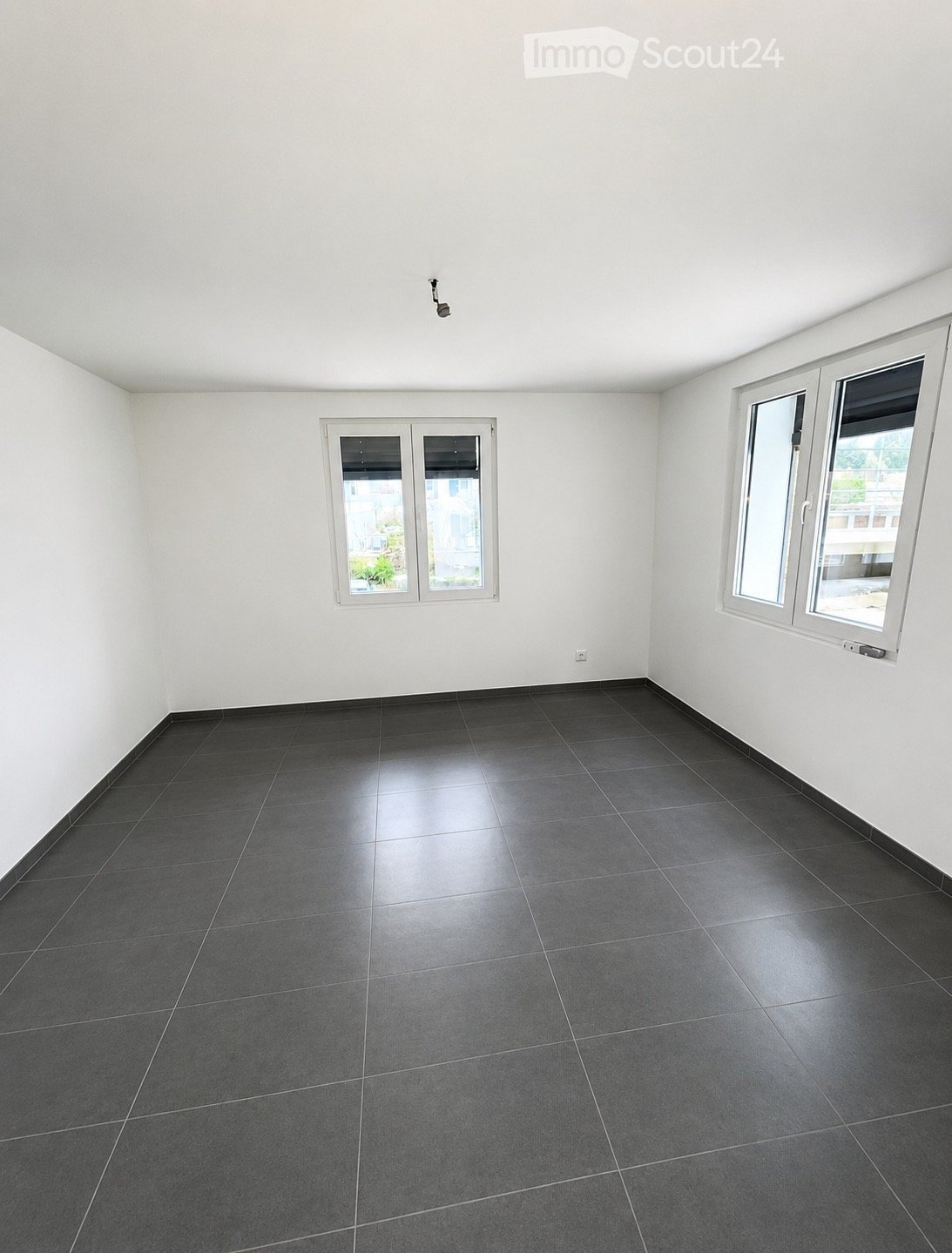 Empty room with white walls, dark tiled floor, and multiple windows providing natural light.