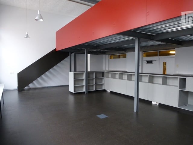 Open-plan unfurnished space with white walls, black floor, white shelving units, and a staircase leading to an upper level.