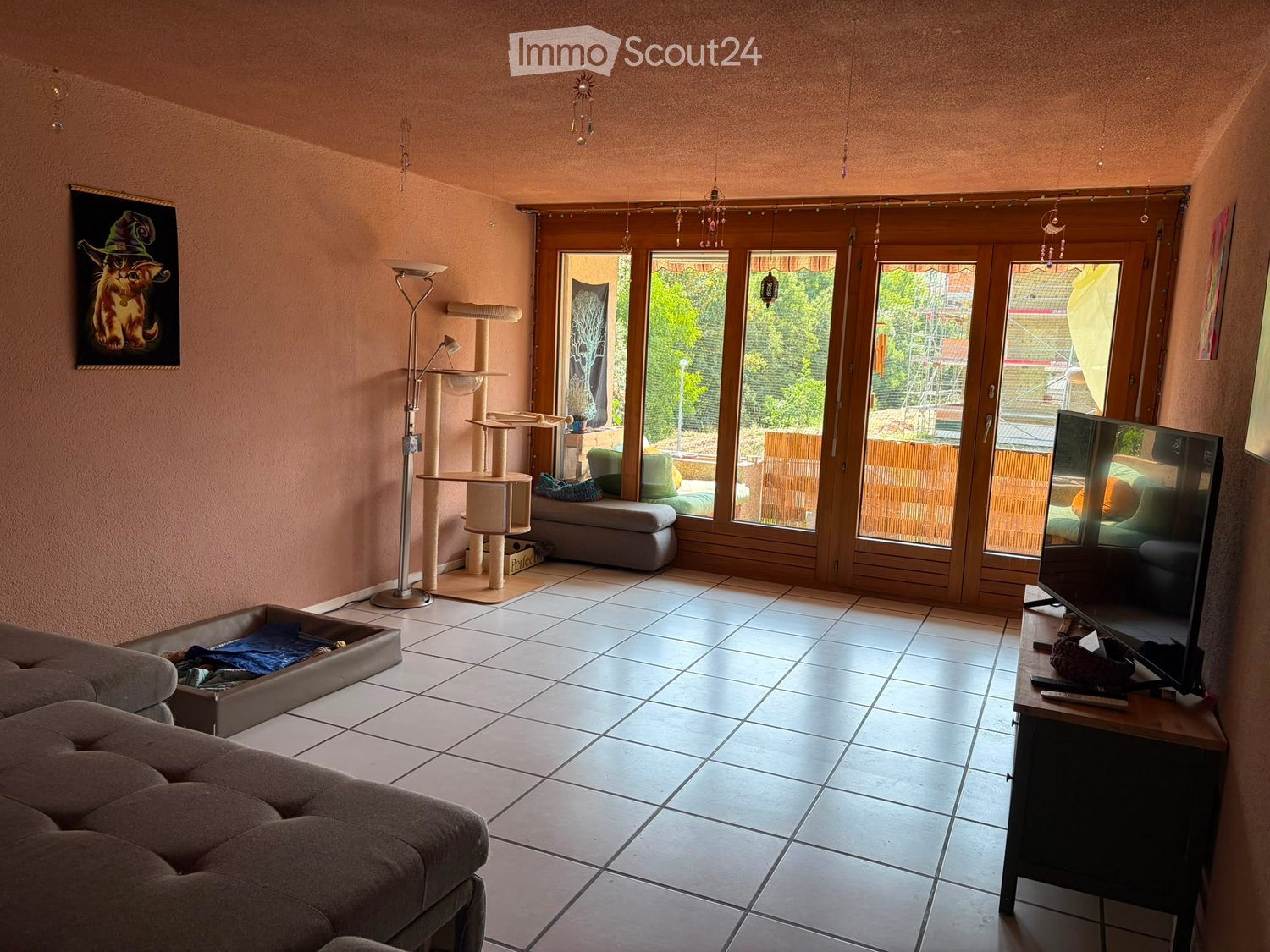 Living room with tiled floor, large windows, cat tree, sofa, television, and a stool.