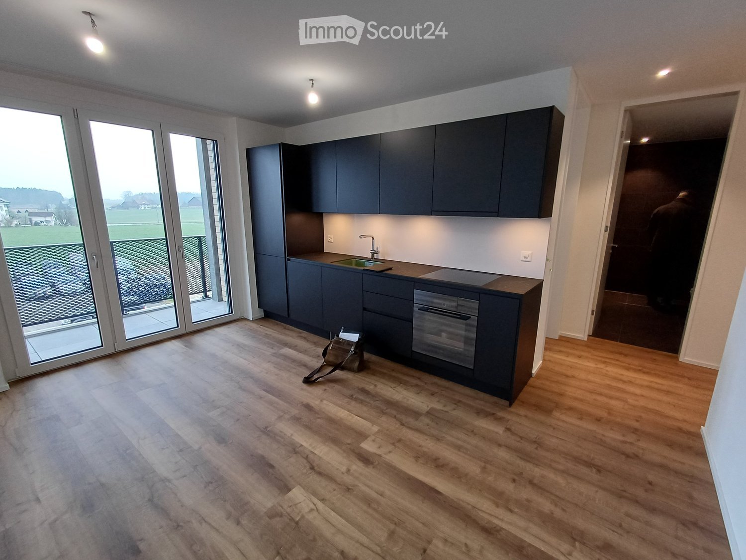 Modern kitchen with dark blue cabinets, a sink, and an oven. The floor is made of light wood, and there is a large window with a view of the outdoors.