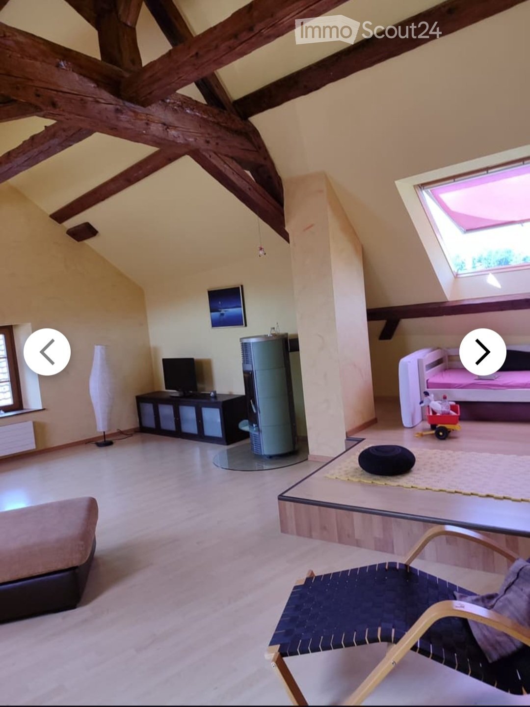 Loft-style room with exposed wooden beams, a sofa, a chair, a table, a TV screen, a cabinet, a stool, and a toy on the floor.