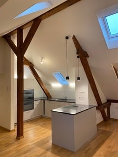 Bright, open-plan attic kitchen with exposed wooden beams, skylights, and modern appliances.