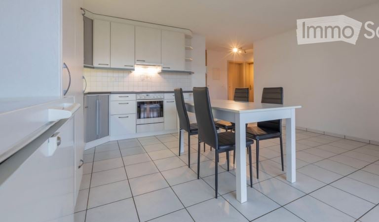 Bright, modern kitchen and dining area with white cabinets, a built-in oven, a refrigerator, and a white dining table with four black chairs.