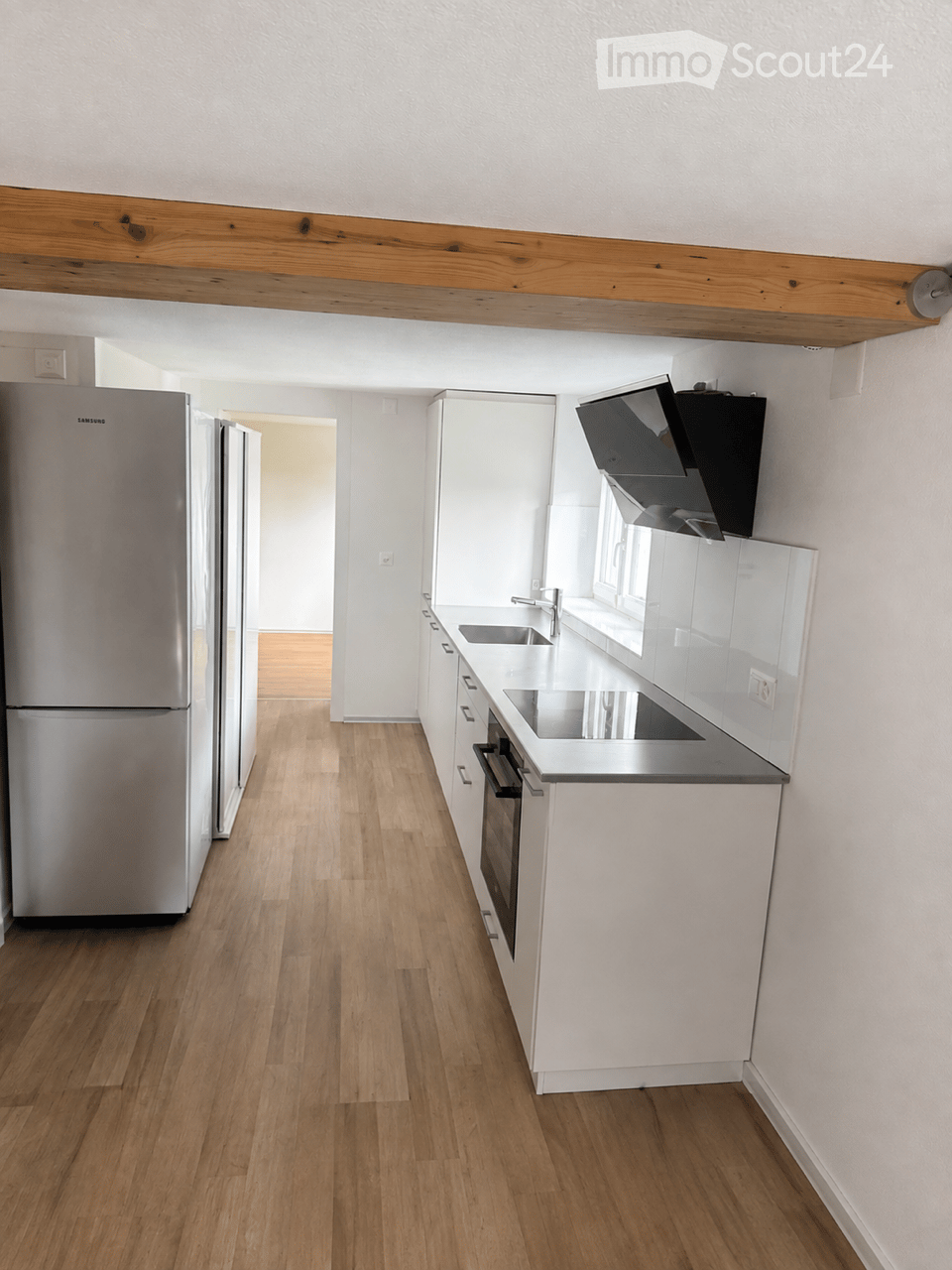 Modern kitchen with white cabinets, stainless steel appliances, wooden flooring, and a visible range hood above the stove.