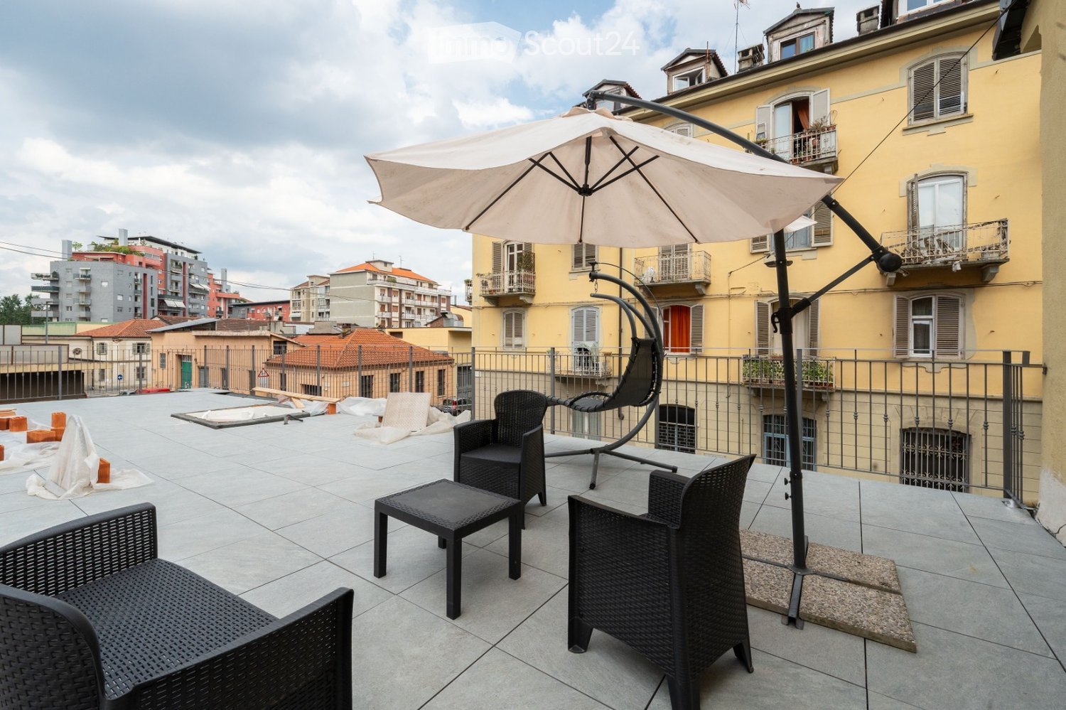 Roof terrace with tiled floor, metal railing, and outdoor furniture including chairs, a table, and a large umbrella.