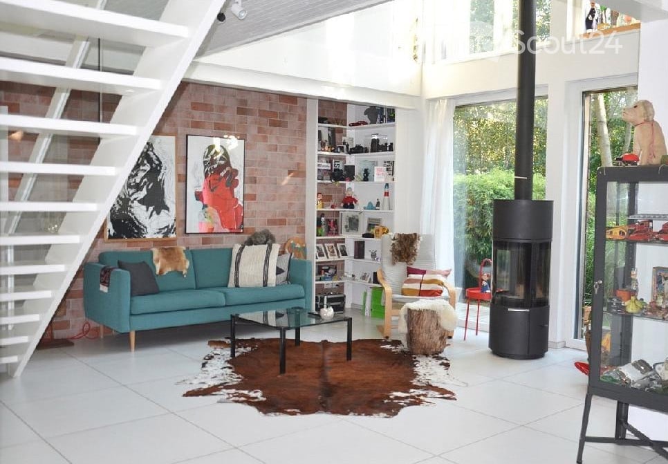 Bright living room with white tiled flooring, teal sofa, glass coffee table, fireplace, and shelves filled with decorative items.
