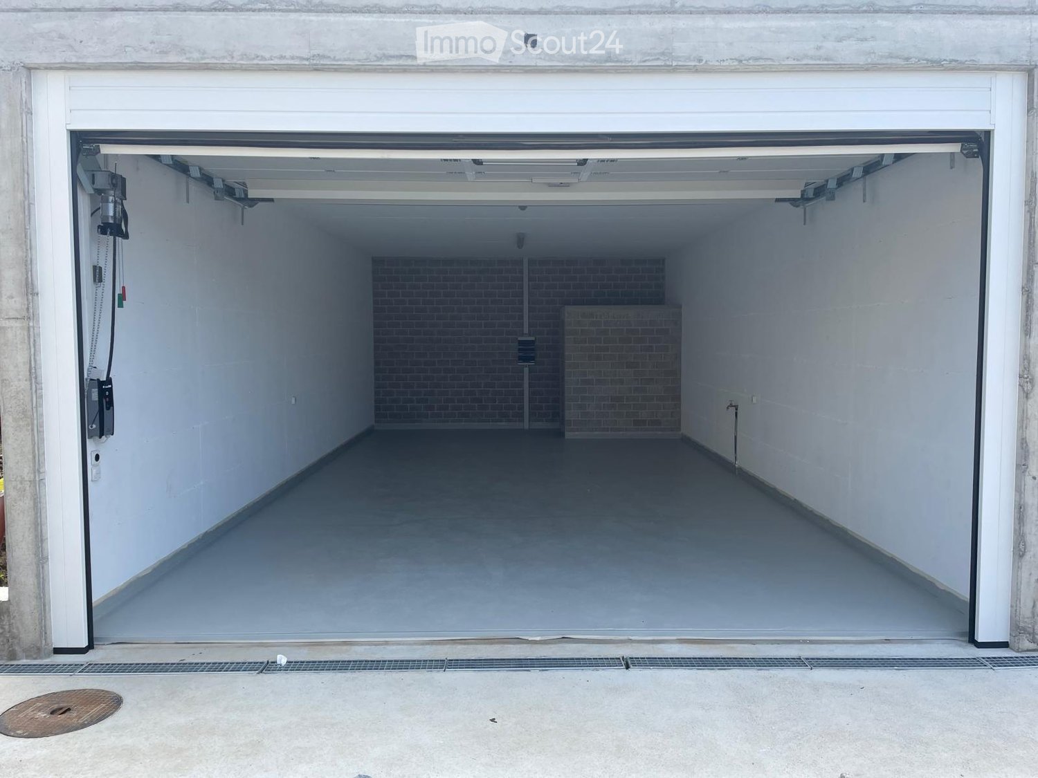 Open garage with concrete floor, white walls, and a brick pillar in the center.
