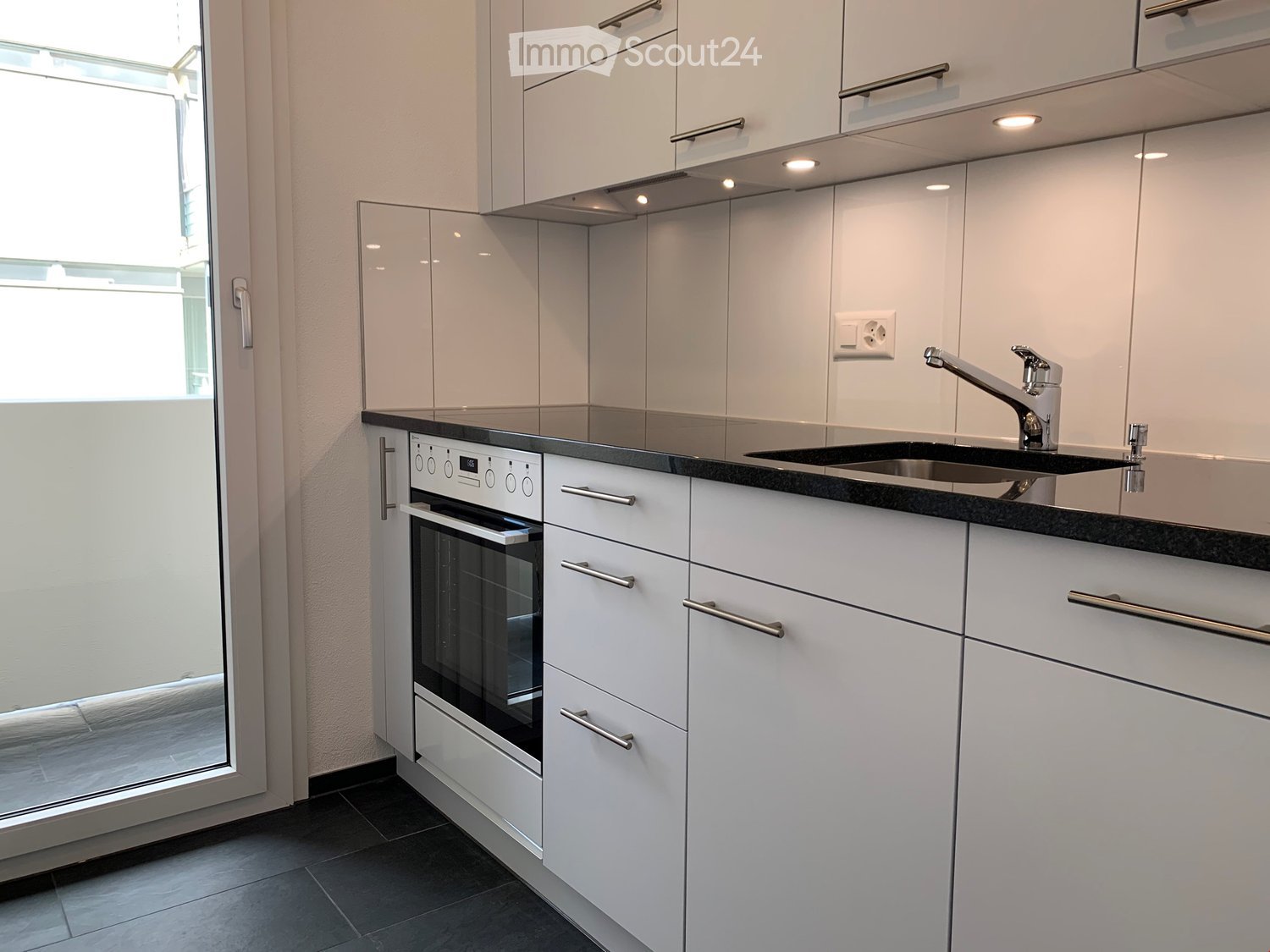 Modern kitchen with white cabinets, black countertop, built-in oven, and stainless steel sink.