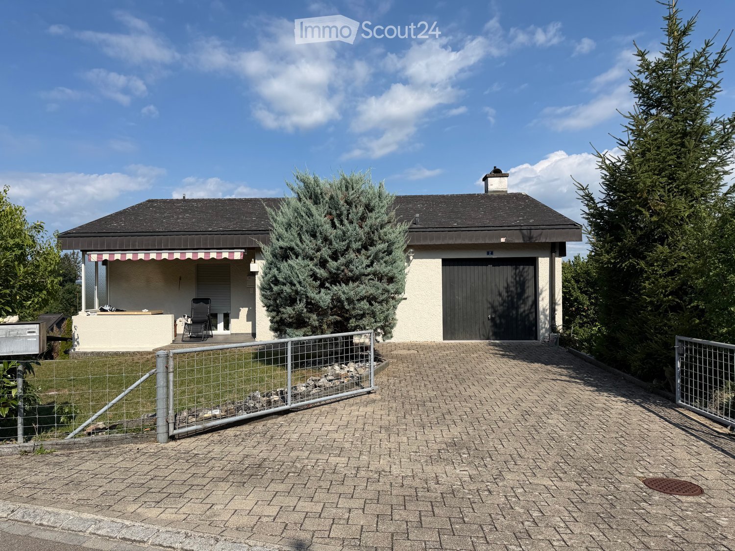 Two-story house with a garage, surrounded by trees and a paved driveway.