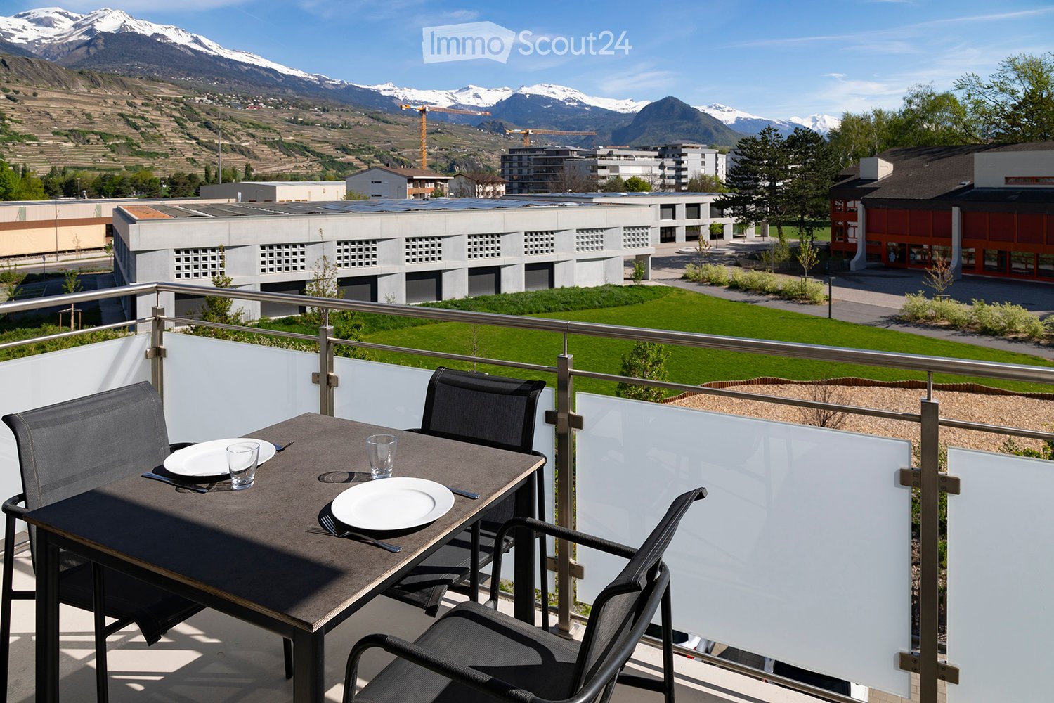 Balcony with a table and chairs, overlooking a green lawn and distant mountains.