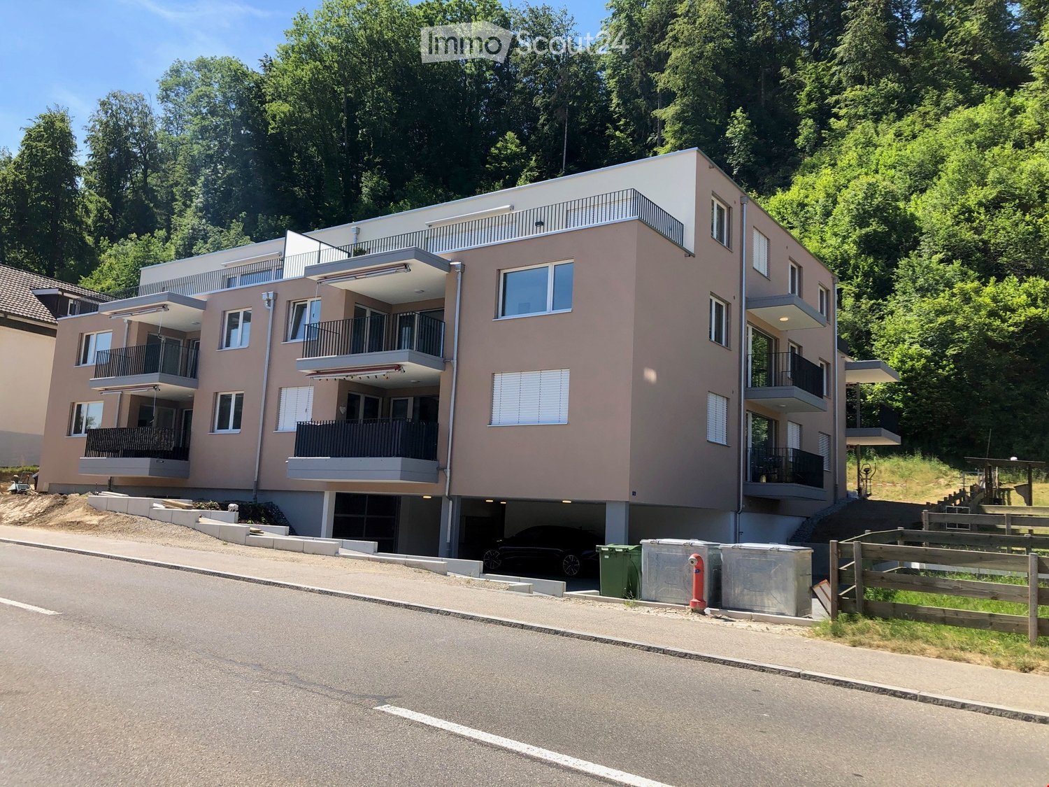 Modern multi-story residential building with balconies, large windows, and a parking area at the base.