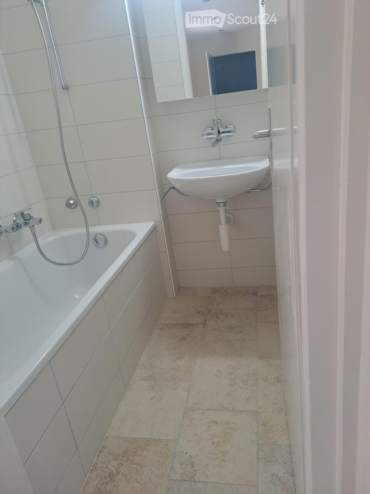 Modern bathroom with a white bathtub, a sink with a modern faucet, and a mirror above the sink. The floor is tiled with beige tiles.