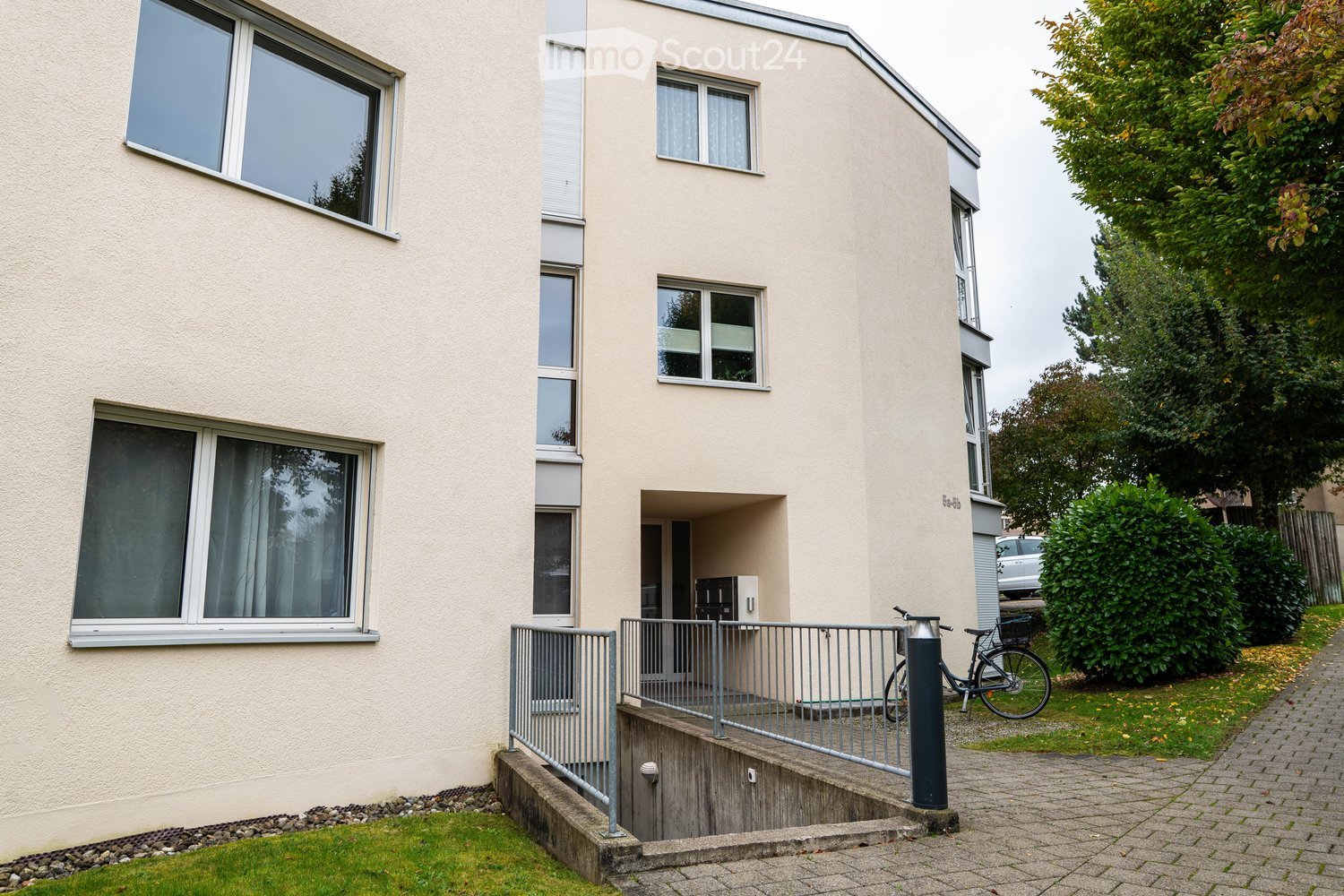 A three-story beige building with windows and a metal railing, garage with a bicycle parked