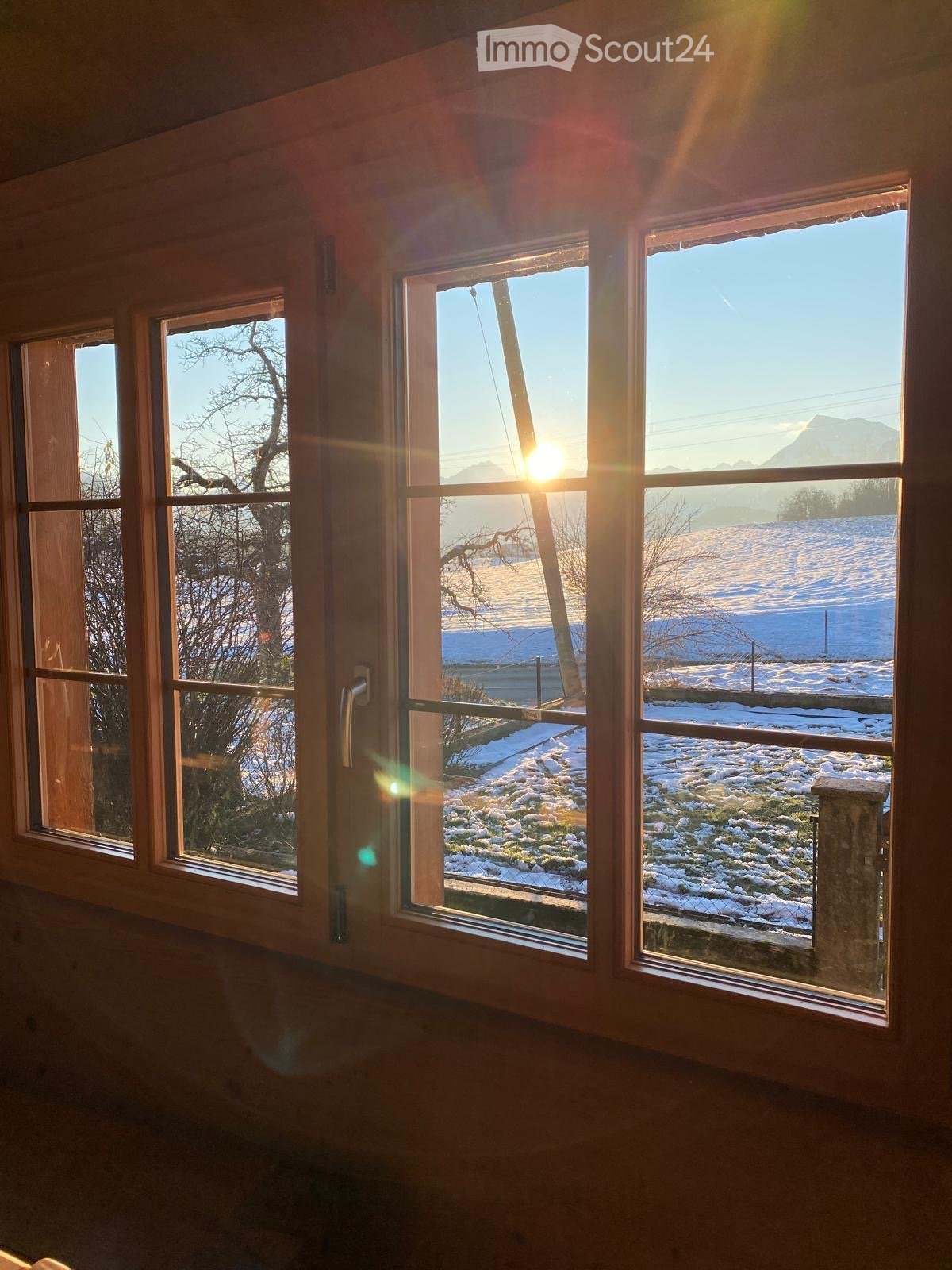 Bright unfurnished room with large windows offering a scenic view of a snow-covered landscape and mountains.