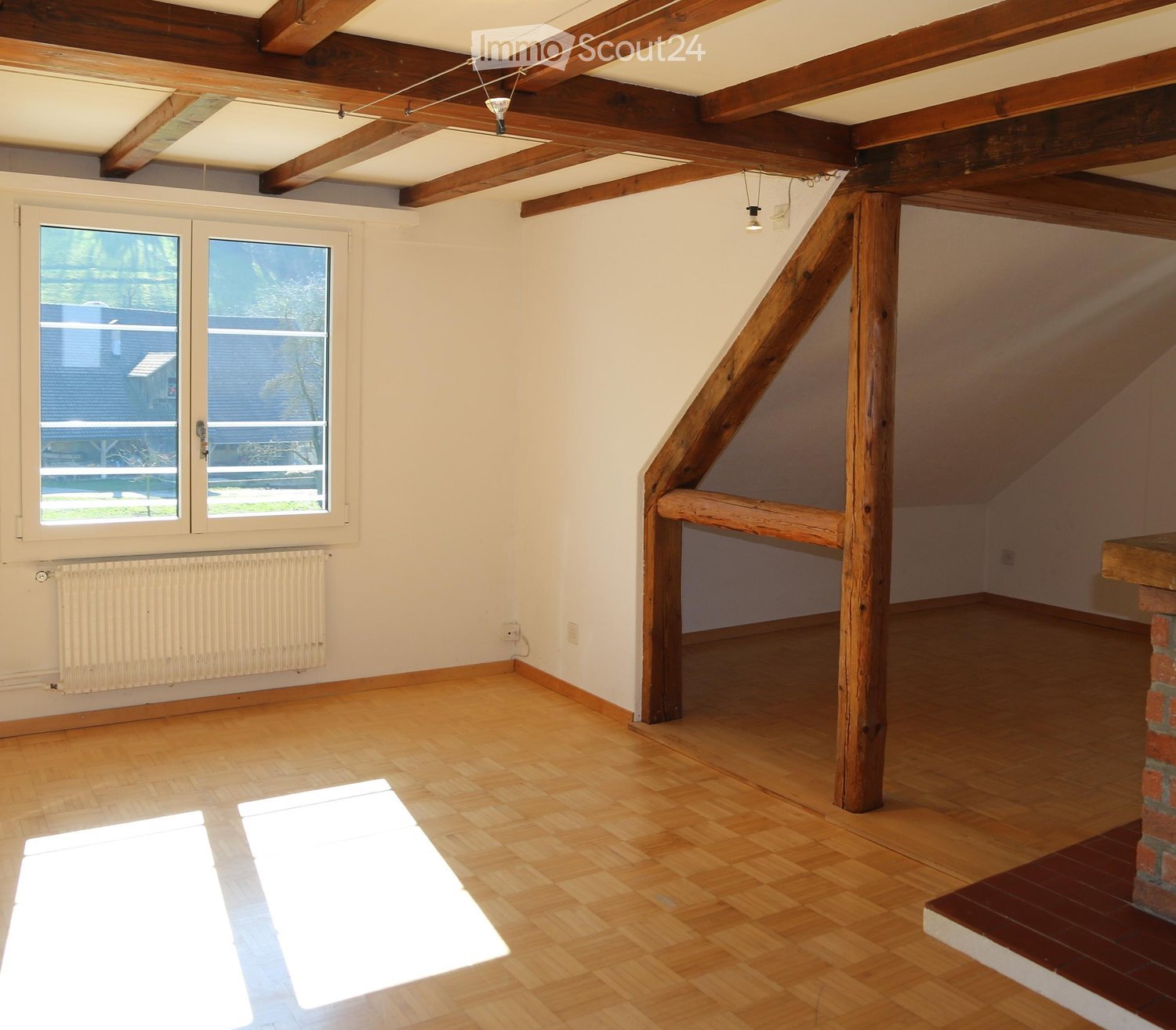 Empty attic room with wooden beams, wooden flooring, large windows, and exposed wooden beams on the ceiling.