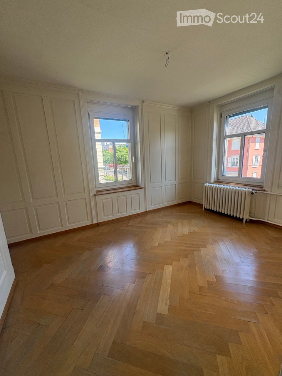 Empty room with wooden flooring, white walls, and two windows with radiators beneath them.