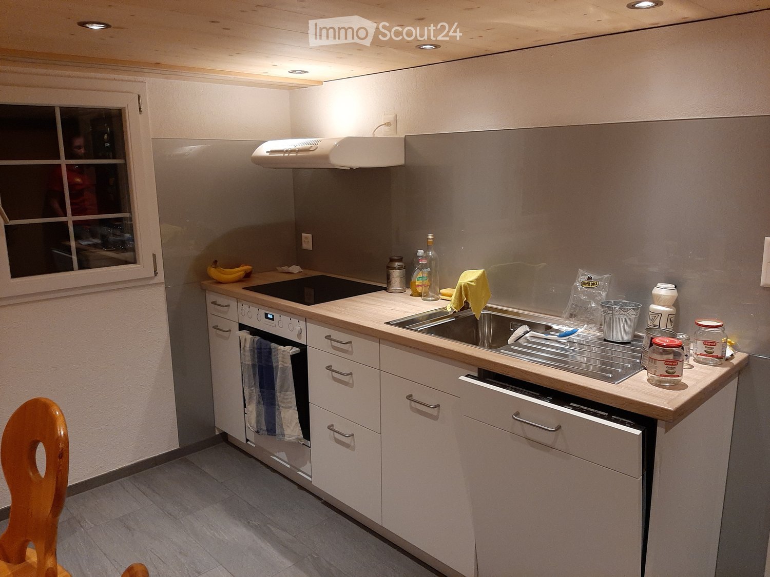 Modern kitchen with white cabinets, stainless steel sink, built-in oven, and various kitchen items on the counter.