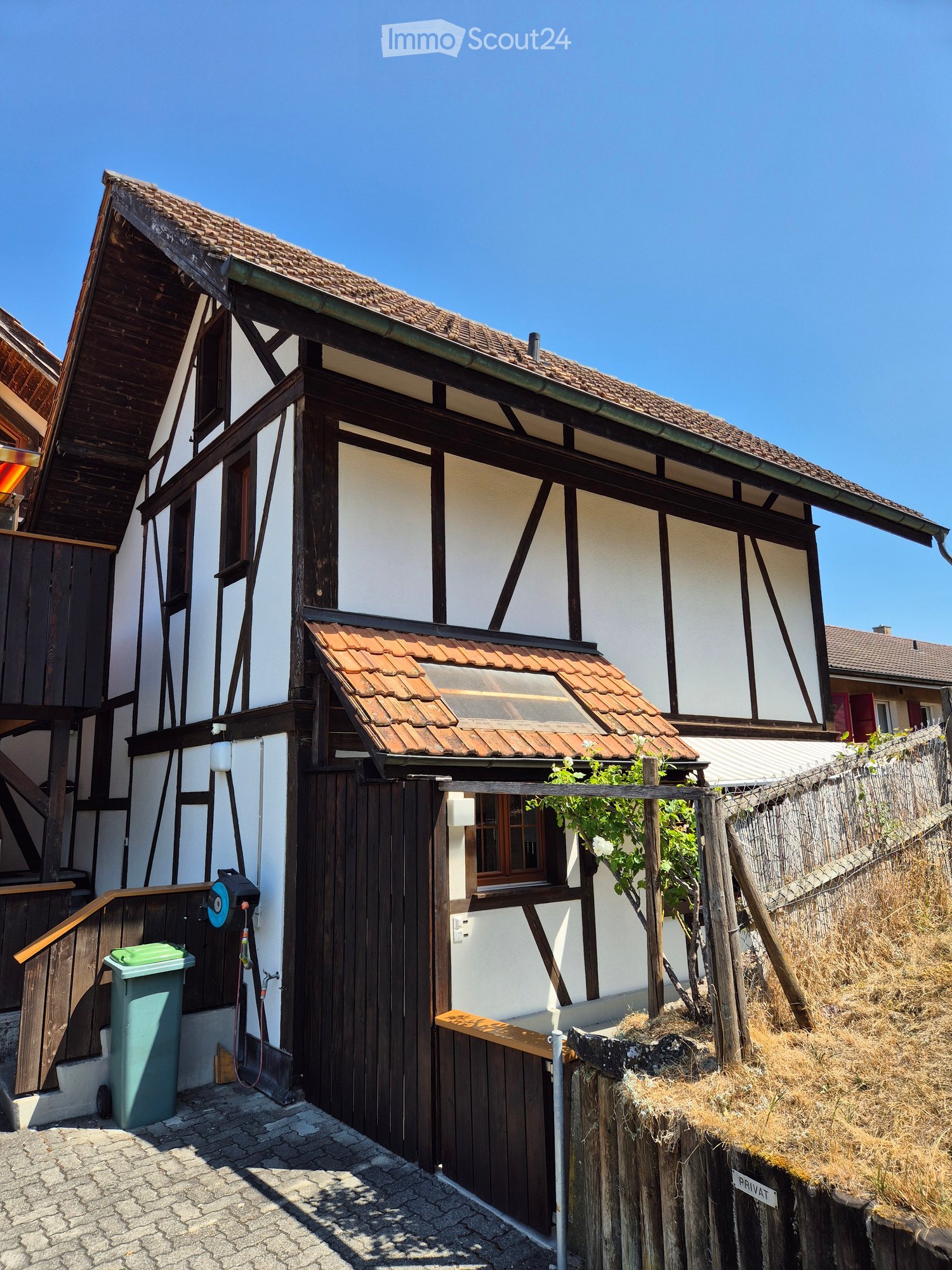 Traditional half-timbered house with white plaster walls and dark wooden beams, featuring a tiled roof and small balcony area.