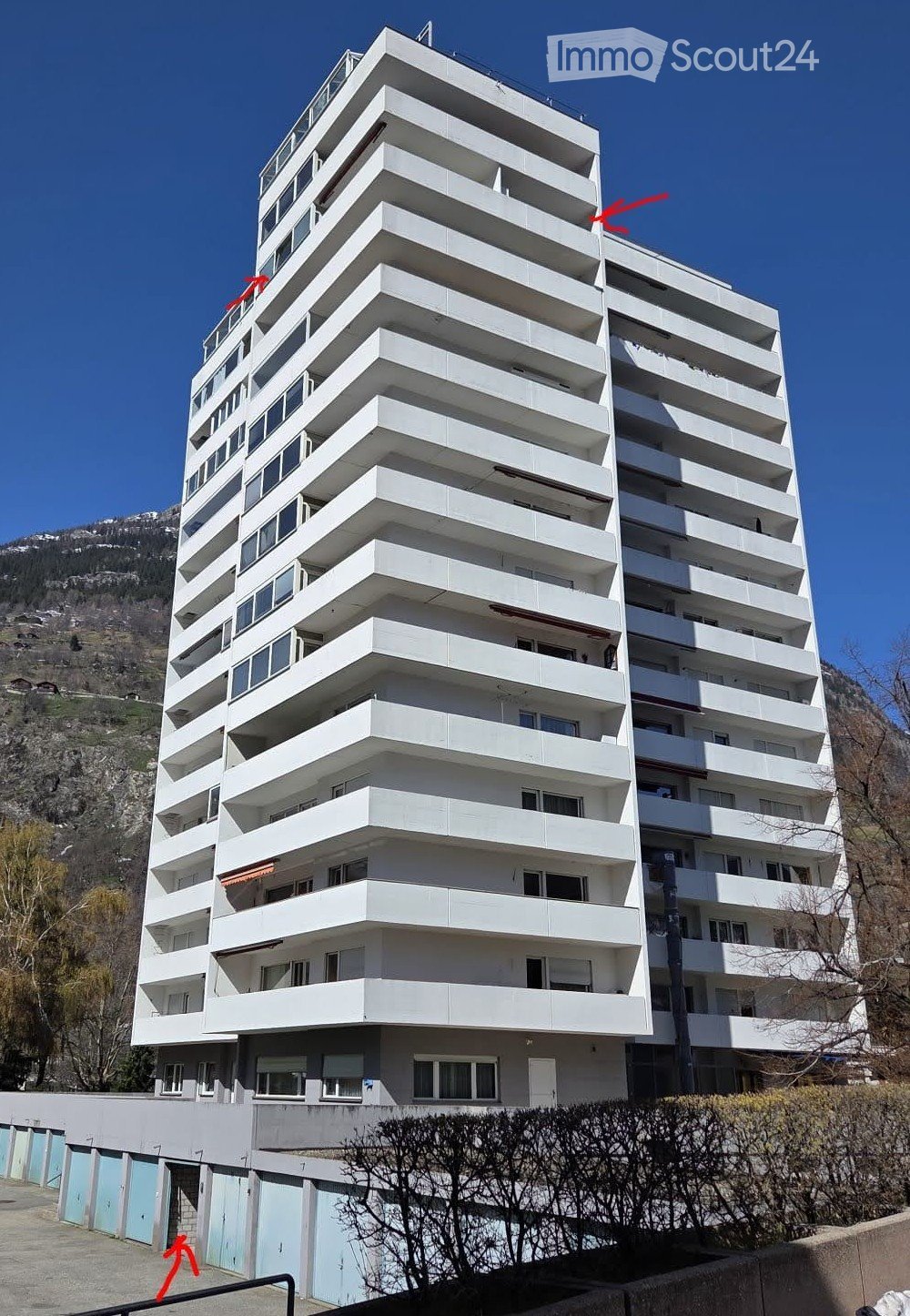 Building. Modern multi-story apartment building with white balconies and large windows, set against a mountainous backdrop.