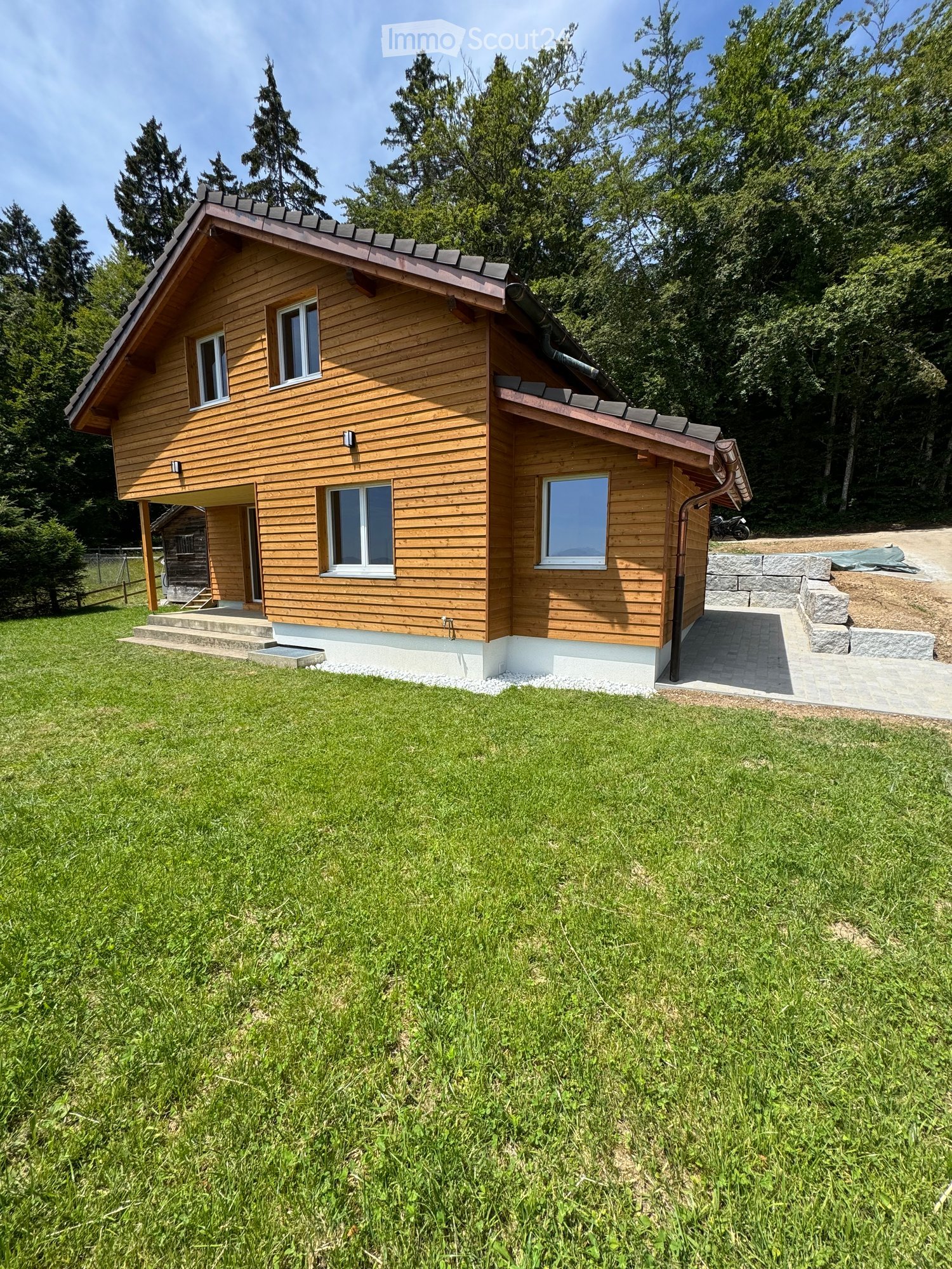 A two-story wooden house with a pitched roof, white trim, and multiple windows, surrounded by a well-maintained lawn and trees.