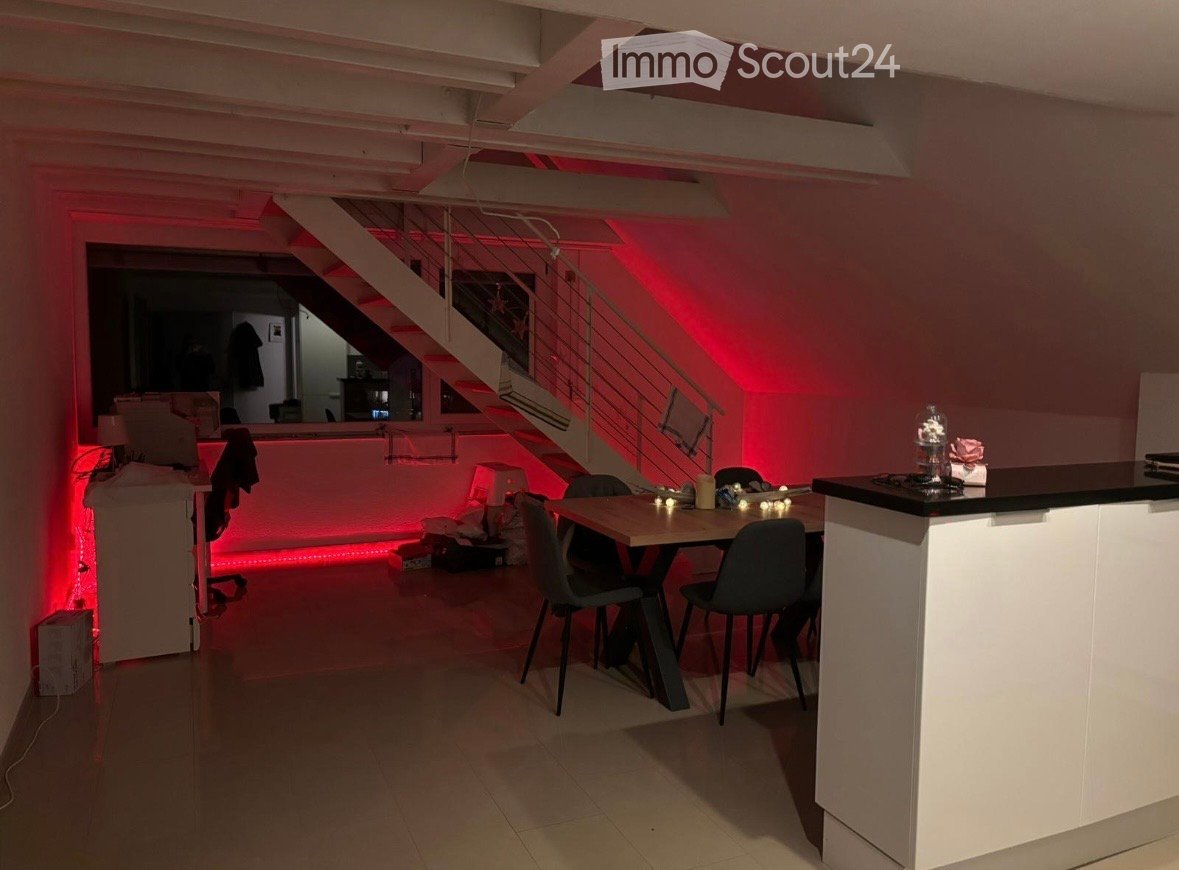 Modern open-plan living and dining area with a staircase leading to an upper level, featuring a dining table with chairs, a kitchen counter, and ambient lighting.