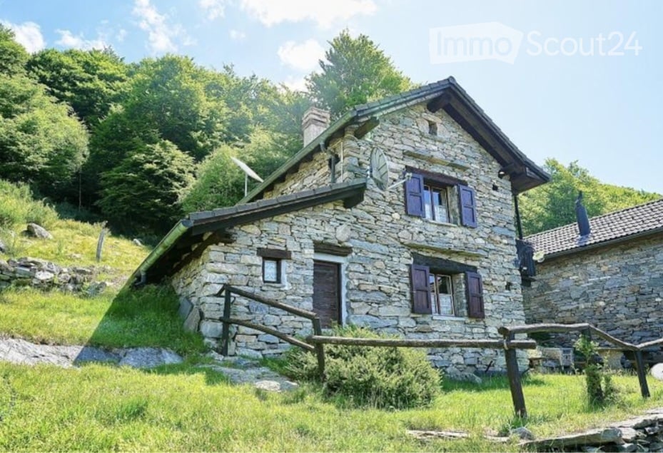 Stone house with a raised ground floor, surrounded by greenery and trees.