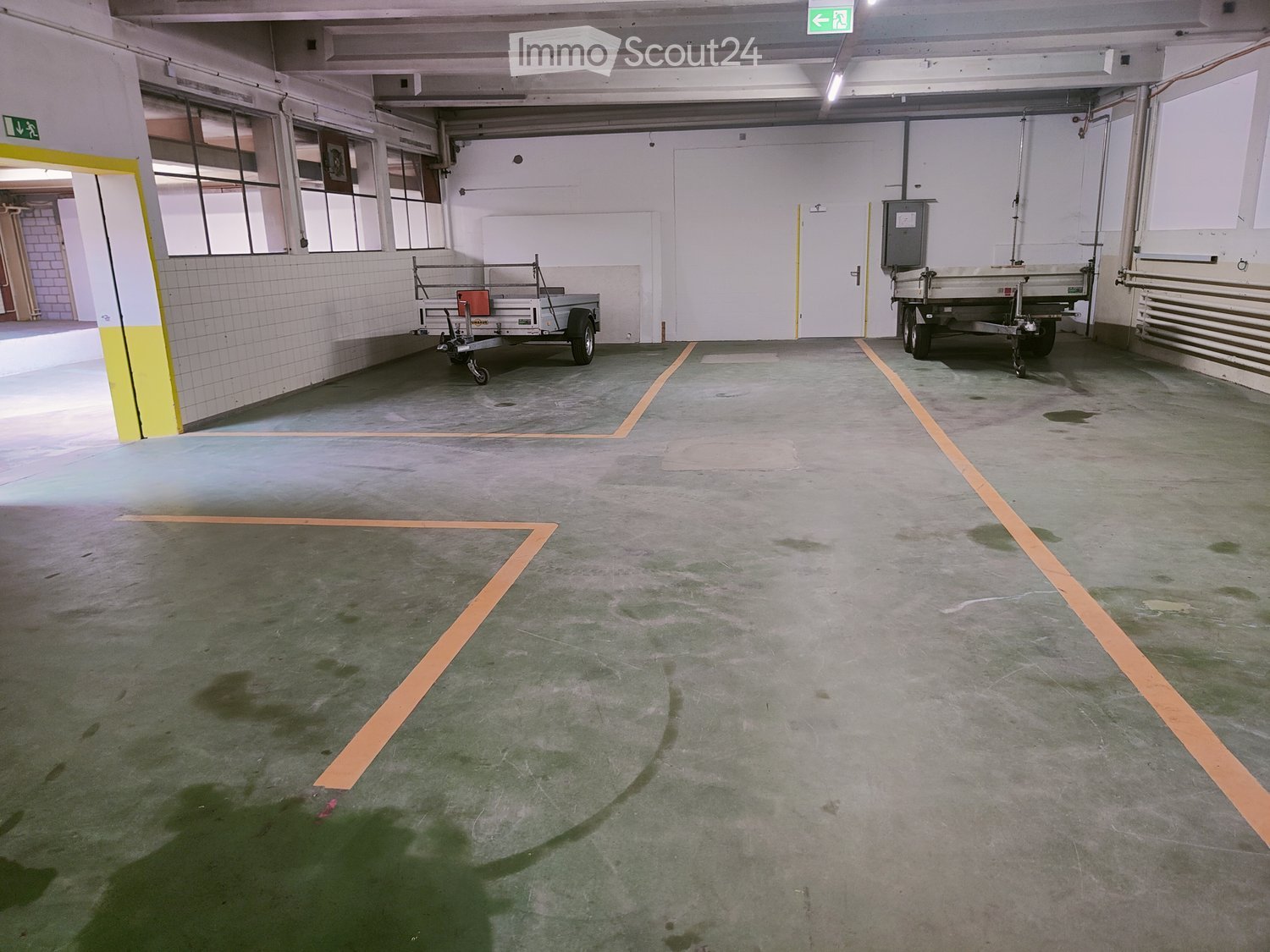 Empty underground parking area with concrete floors, marked parking spaces, and two trailers parked in the background.