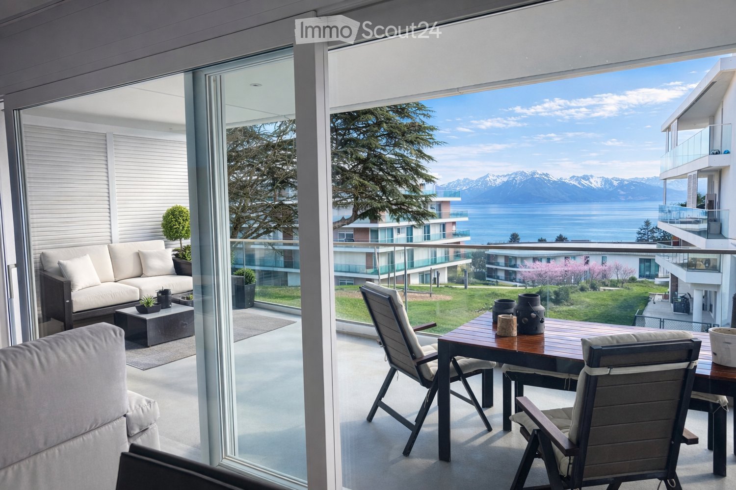 Balcony with a view of a lake and mountains, featuring a sofa, coffee table, and outdoor dining set.