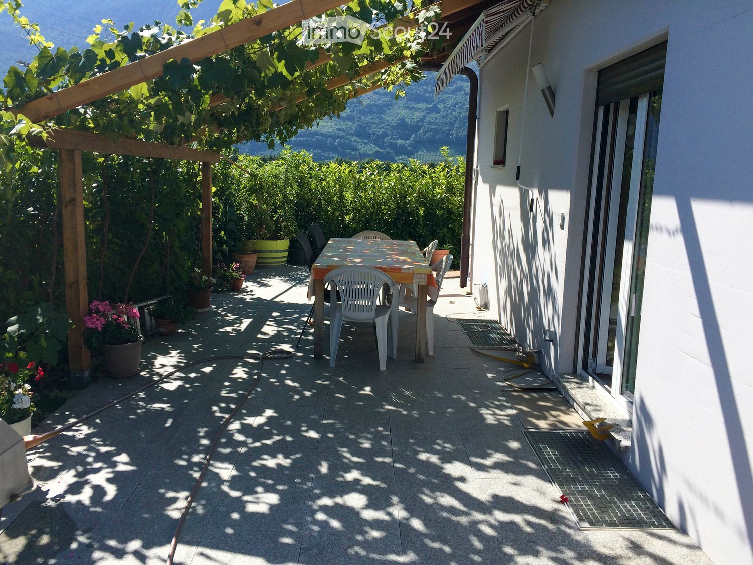 Balcony with a table and chairs, surrounded by greenery and a scenic mountain view.