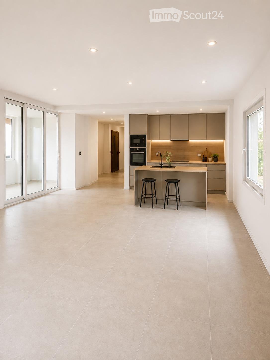 Modern kitchen with light-colored tiles, an island with two stools, built-in appliances, and ample natural light from large windows and sliding doors.