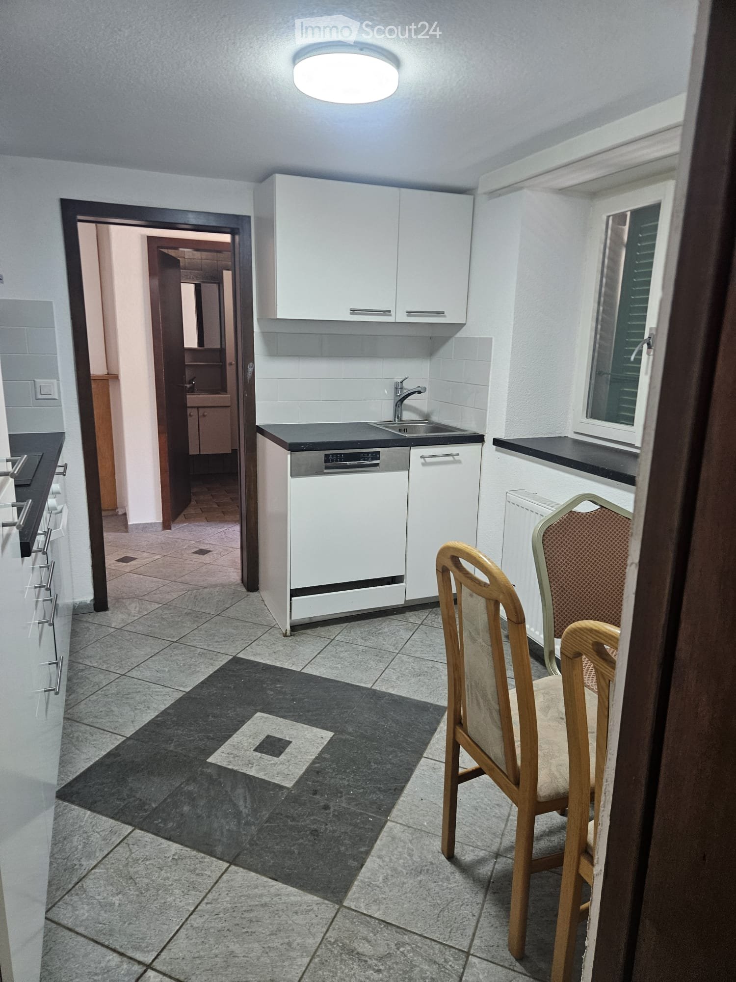 Modern kitchen with white cabinets, a dishwasher, sink, and two wooden chairs near the window.