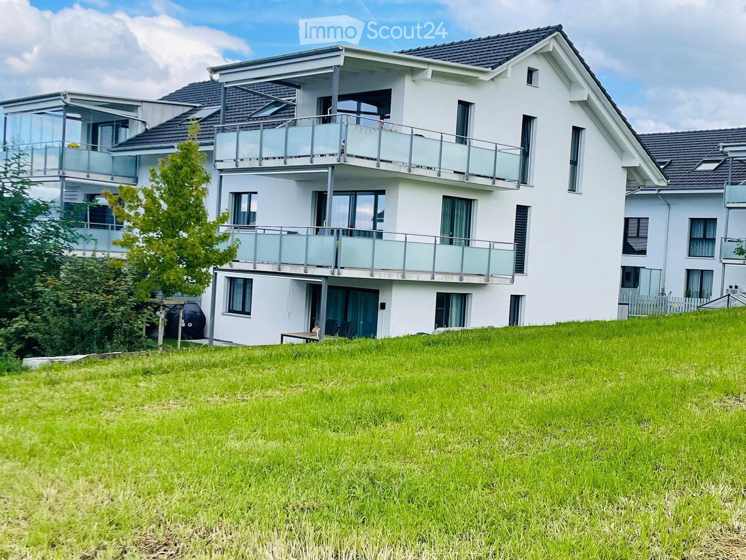 Modern two-story house with white exterior, multiple windows, balconies, and a well-maintained lawn in front.