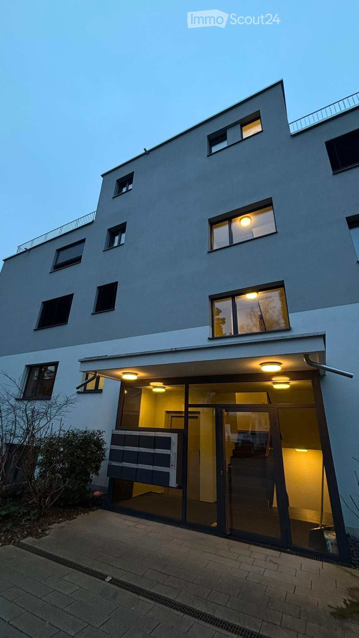 Modern two-story house with large windows, illuminated interior, and a raised ground floor entrance.