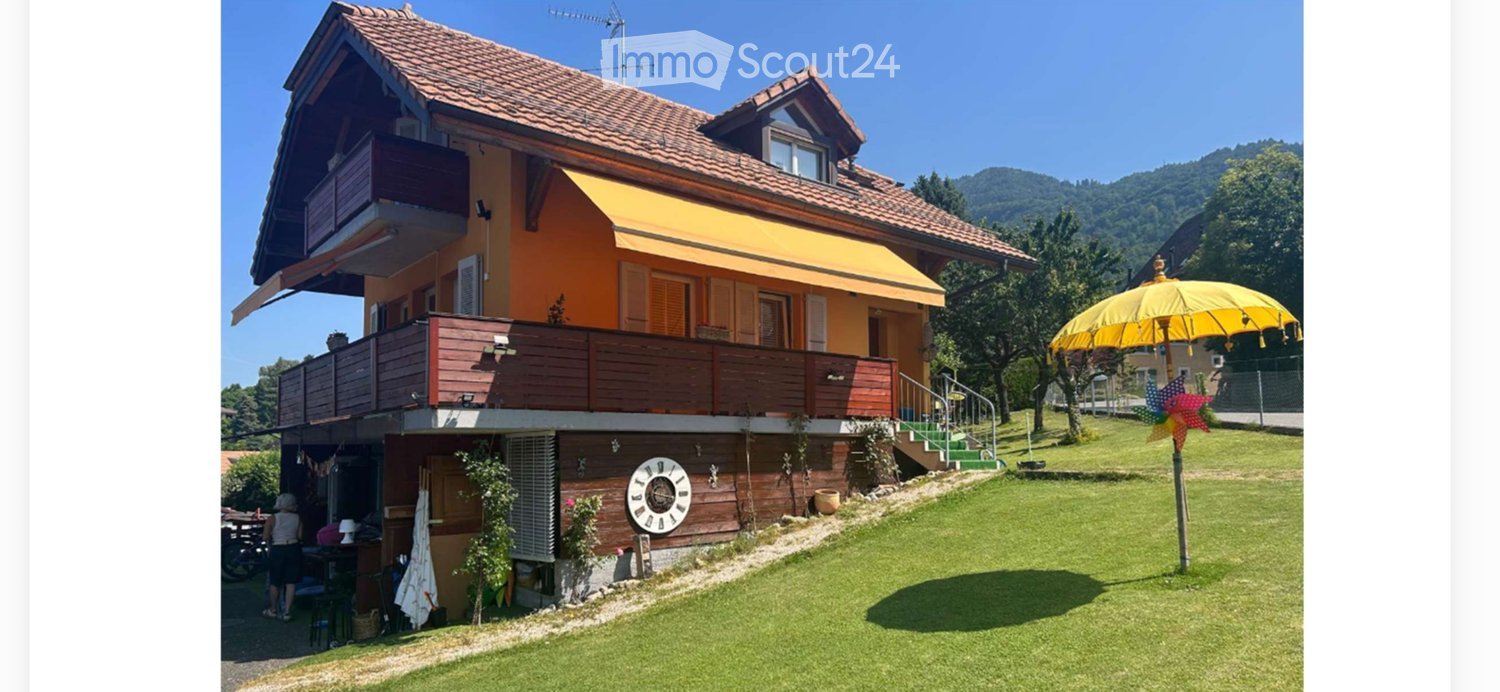 Two-story house with orange facade, wooden balcony, and large front yard with a yellow umbrella and decorative windmill.
