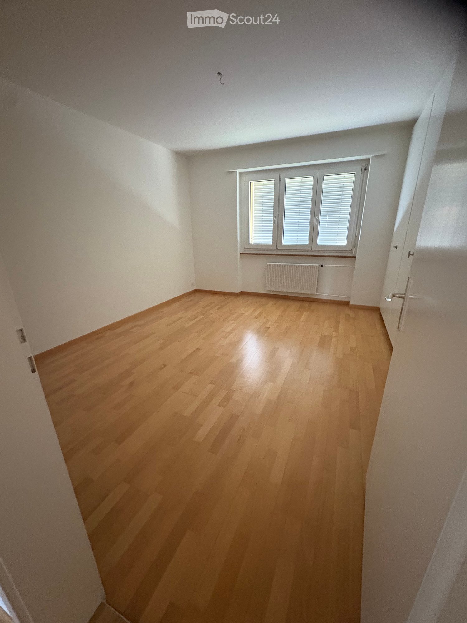 Empty room with wooden flooring, white walls, and a window with blinds. No furniture or equipment is present.