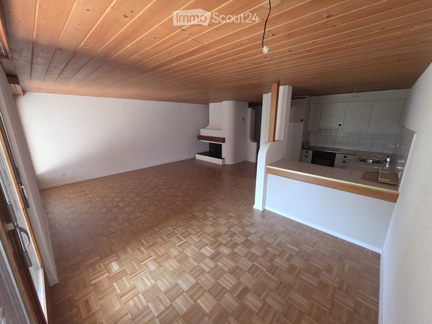 Open-plan living and kitchen area with wooden herringbone flooring, white cabinets, a kitchen counter, sink, faucet, oven, and a fireplace.
