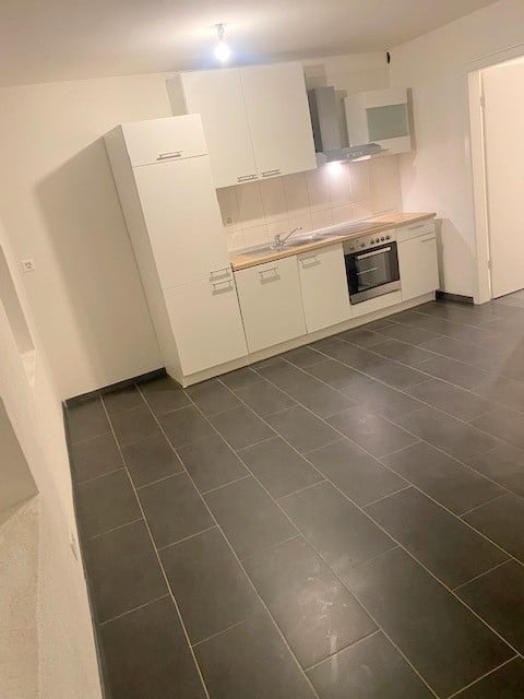 Modern kitchen with white cabinets, dark tiled floor, stainless steel appliances including an oven, microwave, and sink.