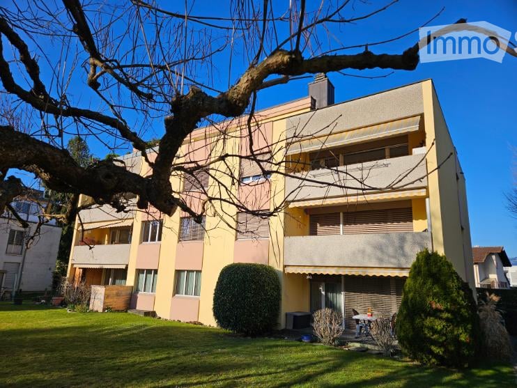 3 story apartment building, yellow and pink exterior, balconies, green lawn, shrubs, tree