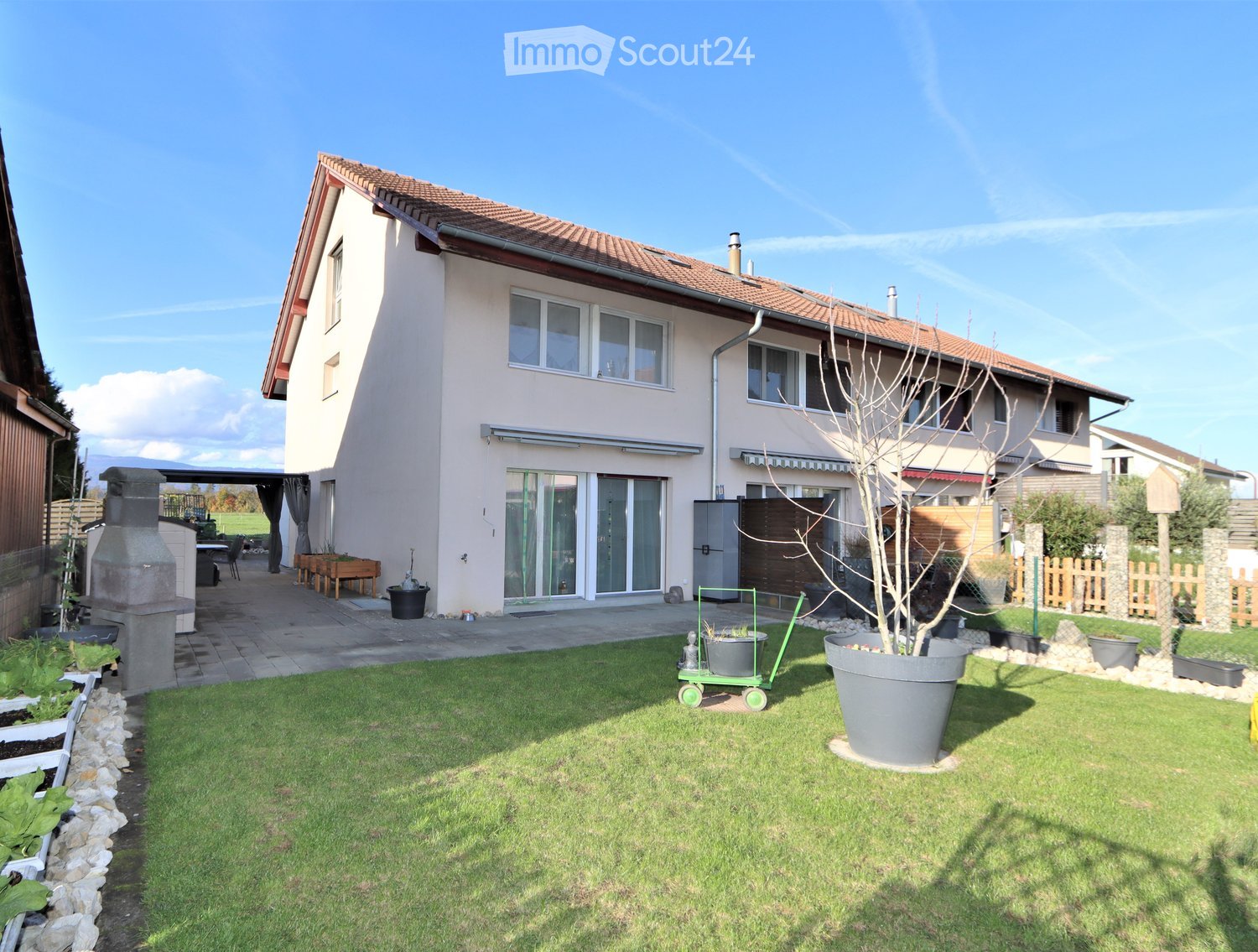 Well-maintained garden with a lawn, potted plants, a barbecue area, and a patio with outdoor furniture.