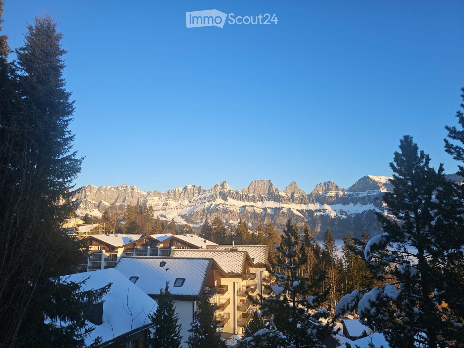 Mountainous area with snow-covered buildings and a snowy mountain range in the background.