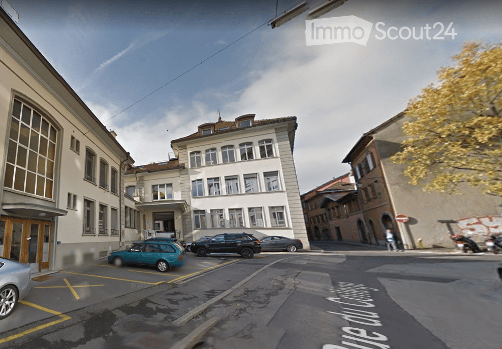 Urban street view with multi-story buildings, parked cars, and a clear sky.